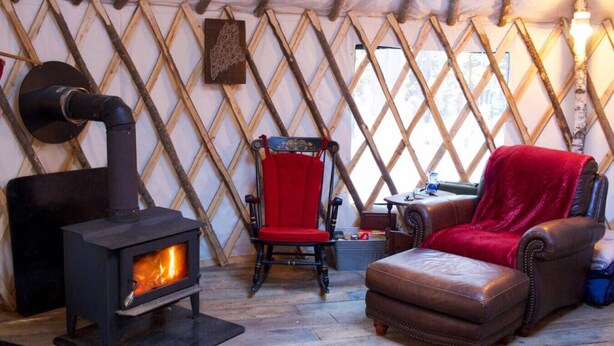 Une pièce chaleureuse avec un poêle à bois, un fauteuil rouge et un pouf en cuir.