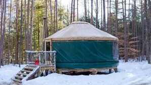 Une yourte recouverte de neige, protégée par une bâche verte, entourée de grands arbres.