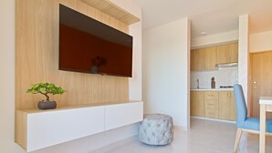 A modern living room with a mounted TV, a small potted plant, a tufted ottoman, and a blue chair. - Primi (Cartagena)