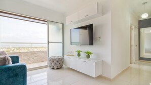 A modern living room with a large window, a flat-screen TV, a white console table, and a teal armchair. - Primi (Cartagena)