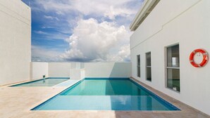 A rooftop swimming pool with clear blue water, surrounded by white walls and large windows. - Primi (Cartagena)