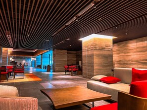 Un vestíbulo moderno con techo de madera, asientos rojos y una lámpara central.