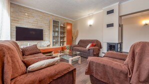 A living room with a flat-screen TV, brown sofas, a glass coffee table, and a brick-patterned wall. - Villa Marijana (Galovac)