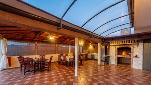 An indoor dining area with a brick floor, wooden tables and chairs, a fireplace, and a glass ceiling. - Villa Marijana (Galovac)