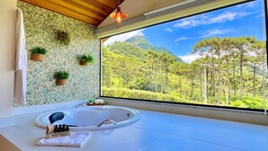 A modern bathroom with a large window, a white bathtub, and a wooden ceiling. - CHALÉS QUINTA DA BOA VISTA  (São Bento do Sapucaí)