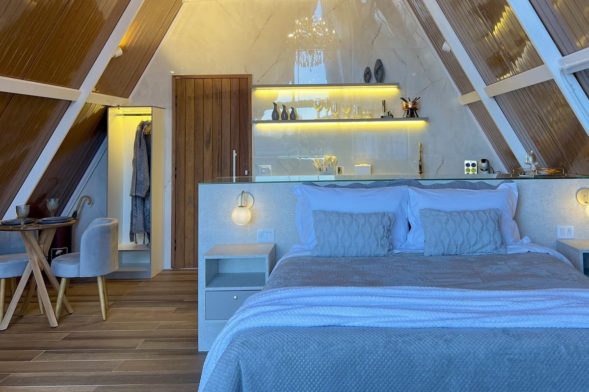 Een moderne slaapkamer met een groot bed, nachtkastjes, een kaptafel met spiegel en een zithoek met een tafel en stoelen.