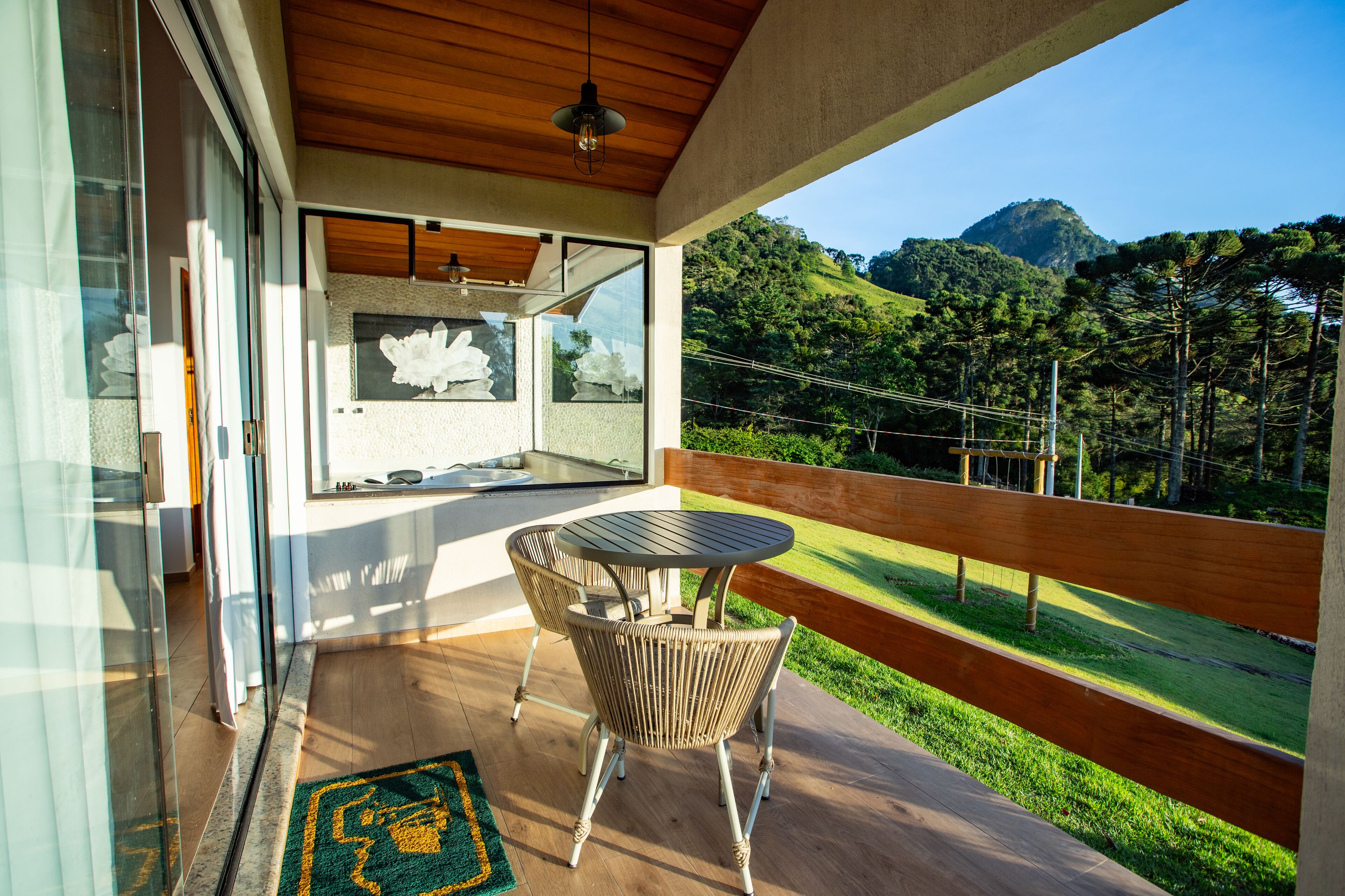 A balcony with wicker chairs and a table, overlooking a lush green landscape and a mountain.
