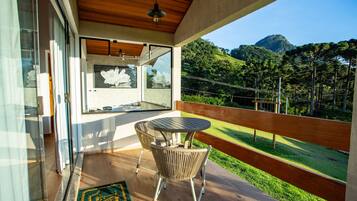 A balcony with wicker chairs and a table, overlooking a lush green landscape and a mountain.