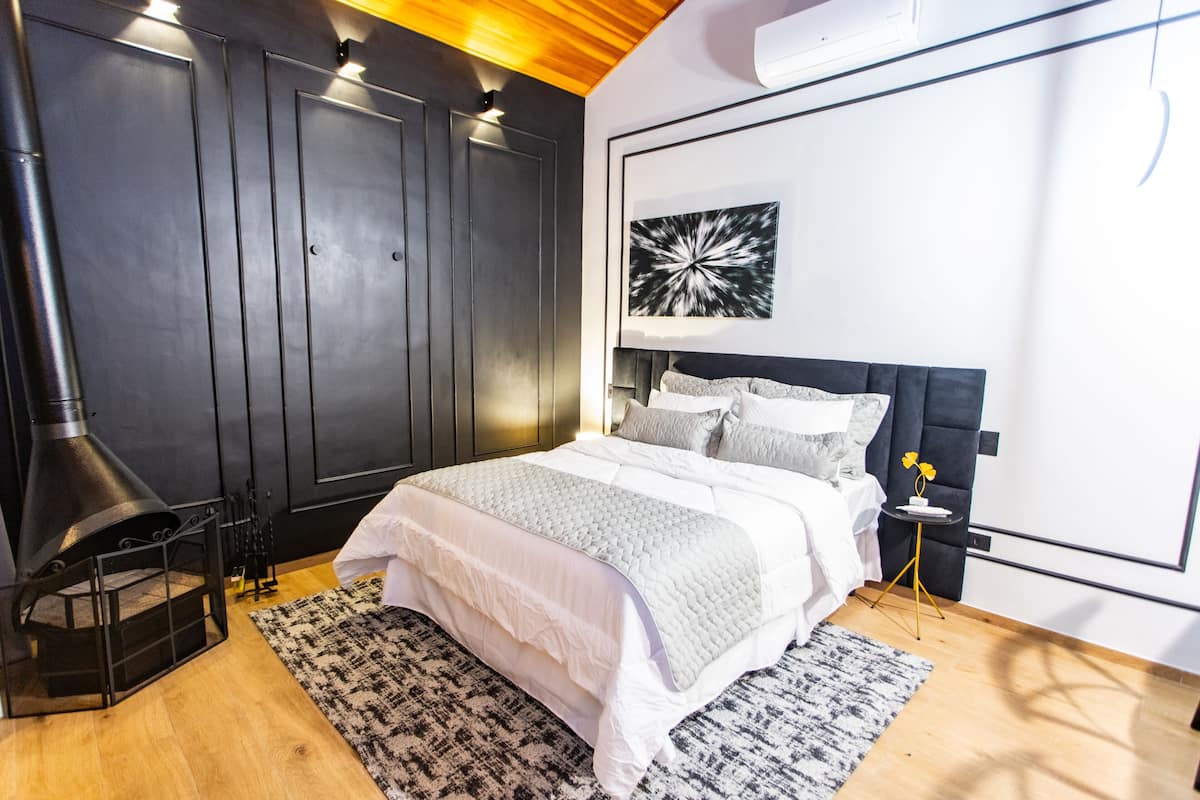 Een moderne slaapkamer met een groot bed, een zwarte garderobe, een open haard en een kunstwerk aan de muur.