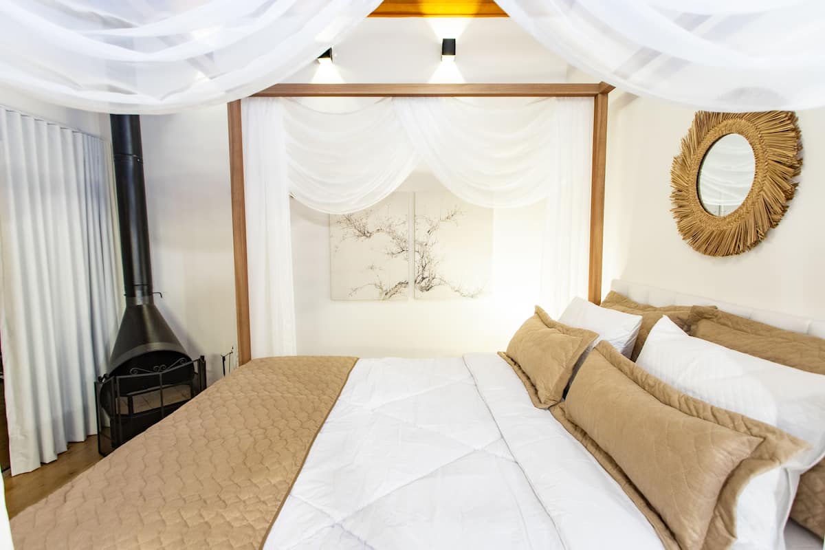 Een slaapkamer met een bed, witte gordijnen, een spiegel aan de muur en een open haard.