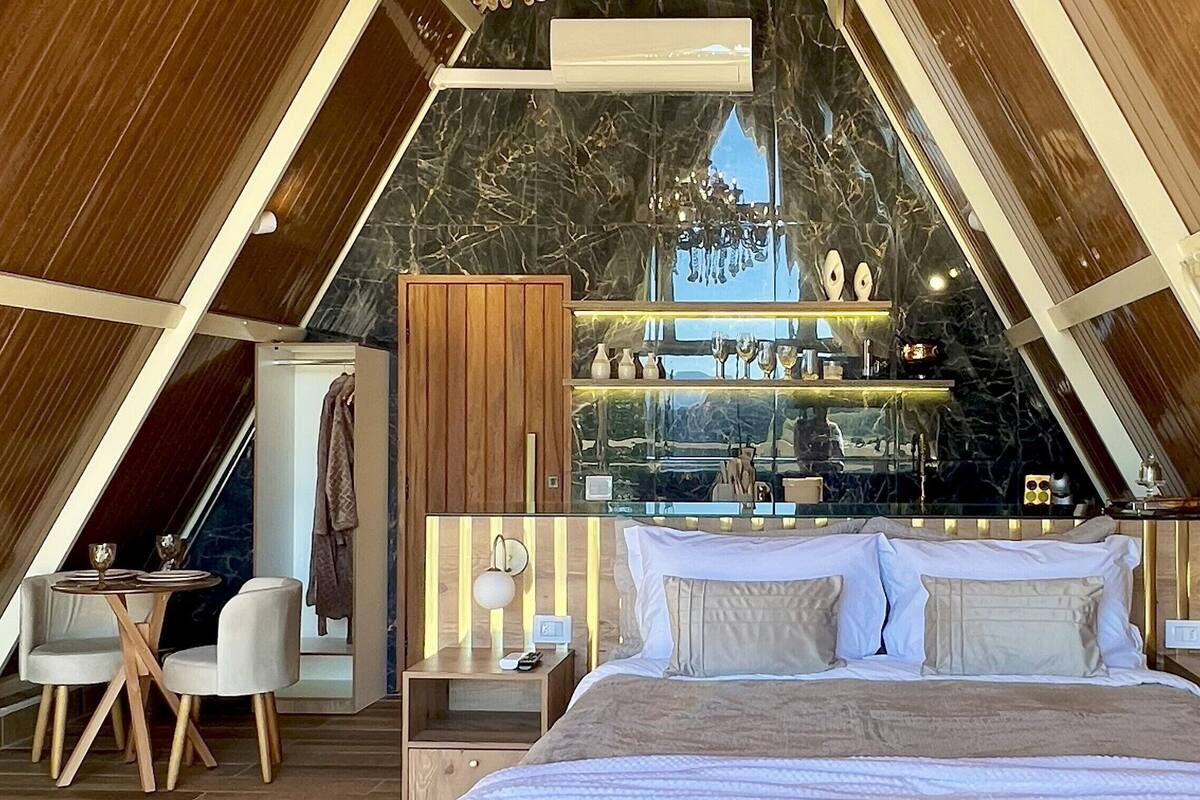 Une chambre moderne de forme triangulaire, comprenant un lit, des tables de chevet et un petit coin salon.