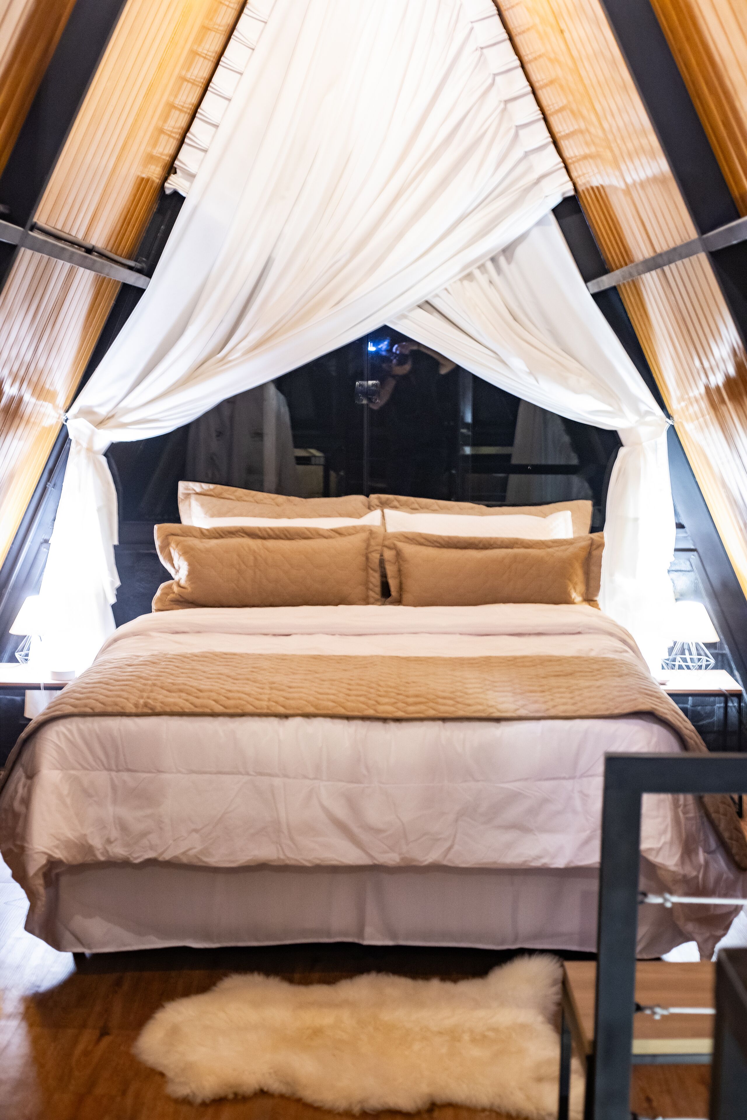 A bed with a canopy, a fluffy rug, and a wooden floor.