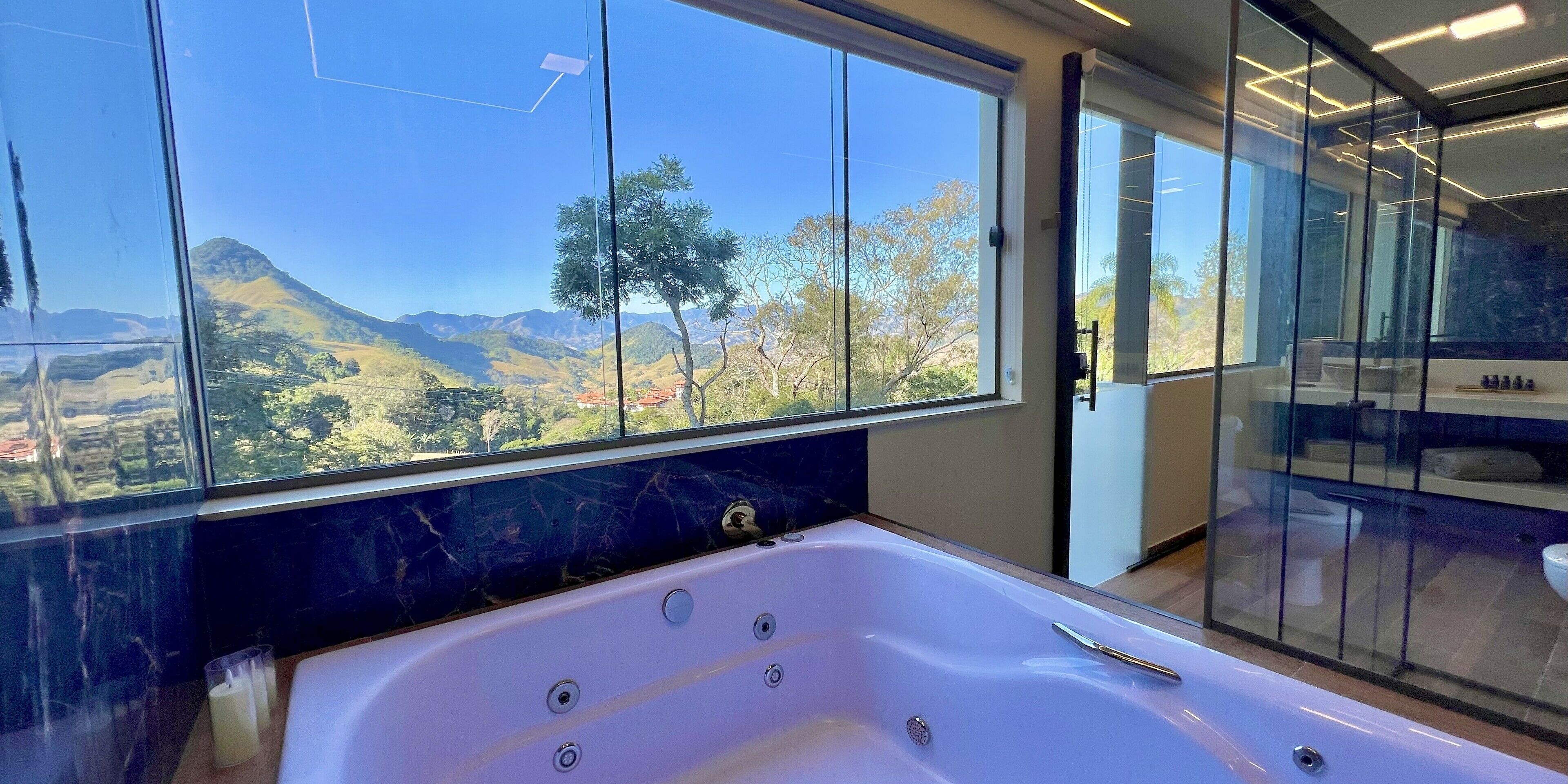 Een moderne badkamer met een groot bad, een douchecabine van glas en uitzicht op een bergachtig landschap.