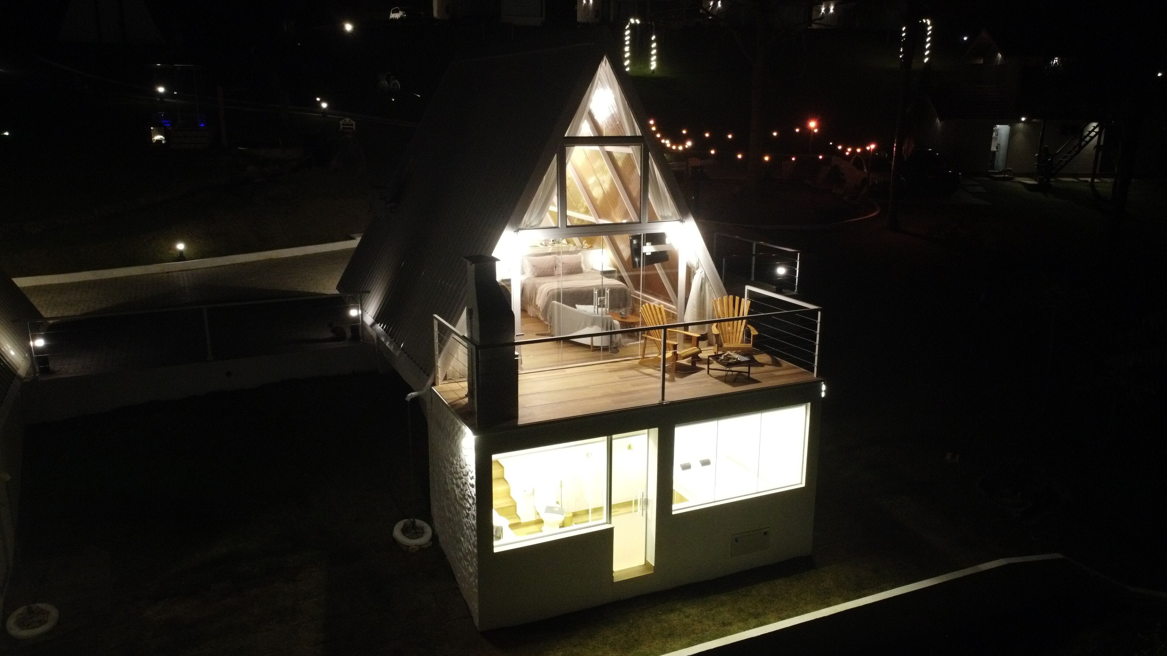 A small, triangular-roofed cabin with a balcony and a visible bedroom.
