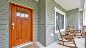 Une maison avec une porte d’entrée en bois, une fenêtre et deux fauteuils à bascule sur le porche.