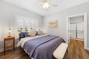 Ein Schlafzimmer mit Bett, Nachttisch, Deckenventilator, Fenster mit Jalousien, einem Bild und einem begehbaren Kleiderschrank.