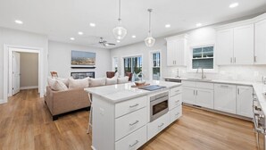 Une cuisine moderne avec des meubles blancs, un îlot central doté d’un four encastré et des luminaires suspendus.