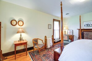 Una camera da letto con un letto a baldacchino, una sedia di legno, un tavolino con una lampada e un tappeto decorativo.