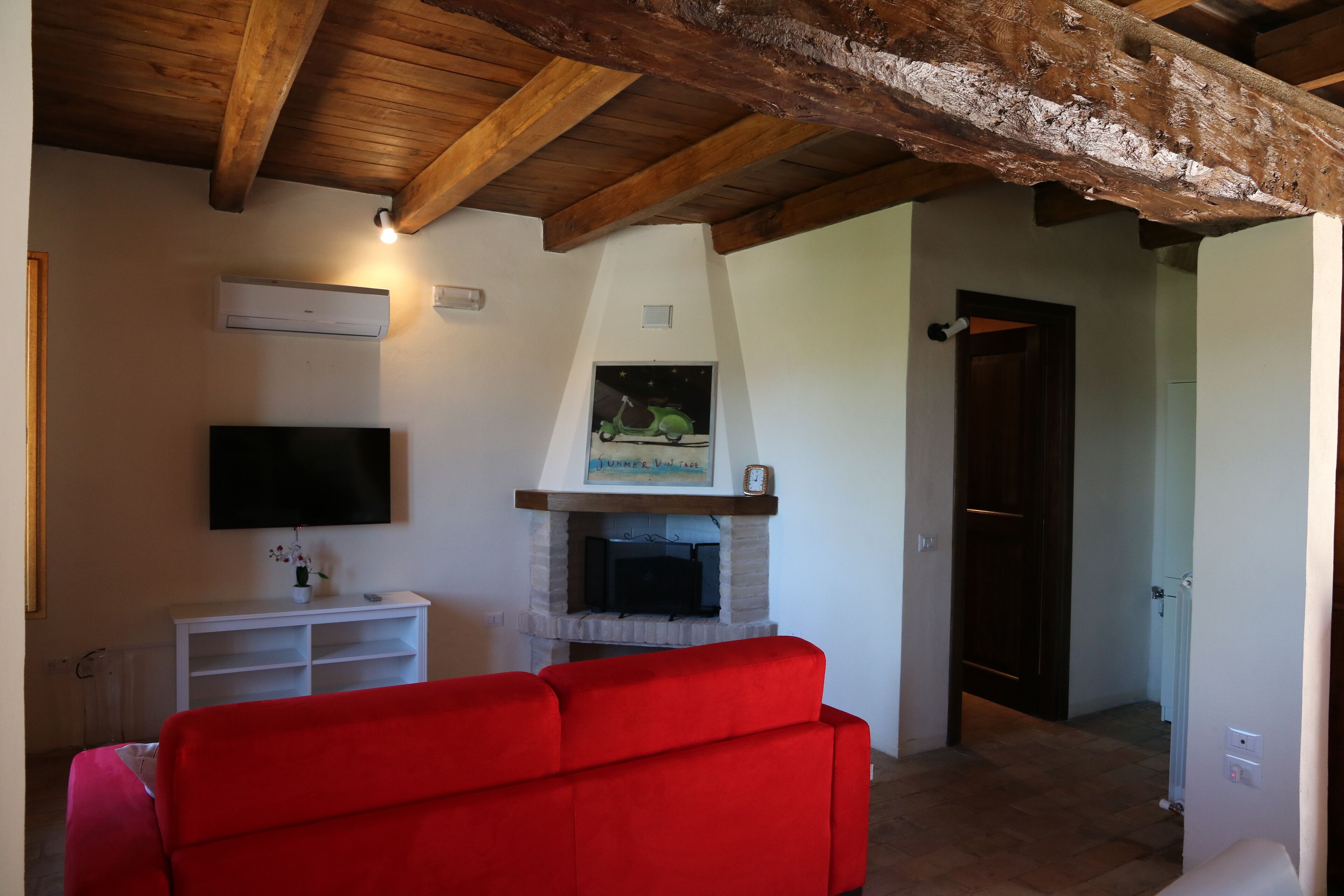 Ein Wohnzimmer mit einem roten Sofa, einem Kamin, einem Wand-Fernseher und Holzbalken an der Decke.