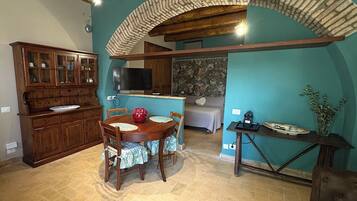Un comedor con mesa y sillas de madera, una cocina con armarios, un televisor y un sofá al fondo.