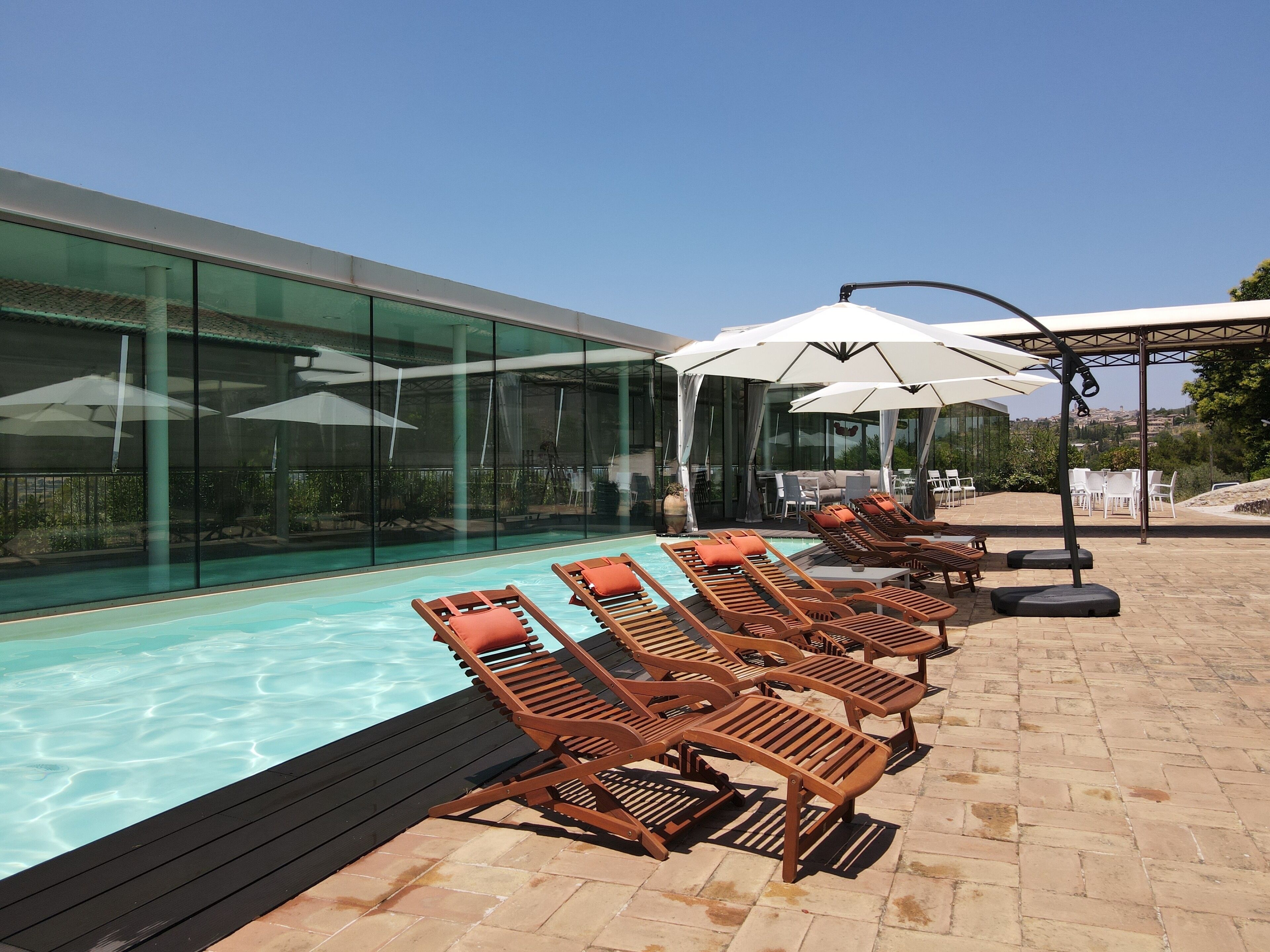 Ein Poolbereich mit Liegestühlen und Sonnenschirmen, eine Glaswand und eine Landschaftsansicht.