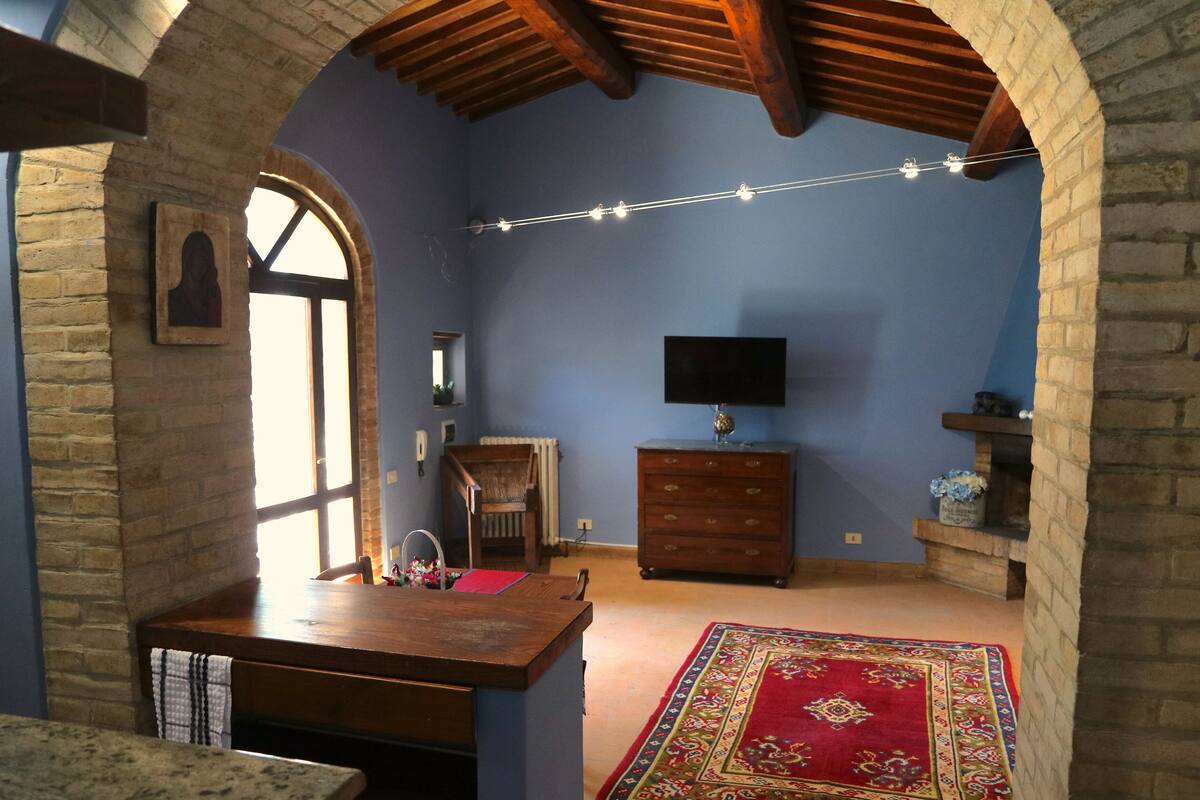 Una habitación con una mesa de madera, un tapete rojo estampado, un televisor y una pared de piedra.