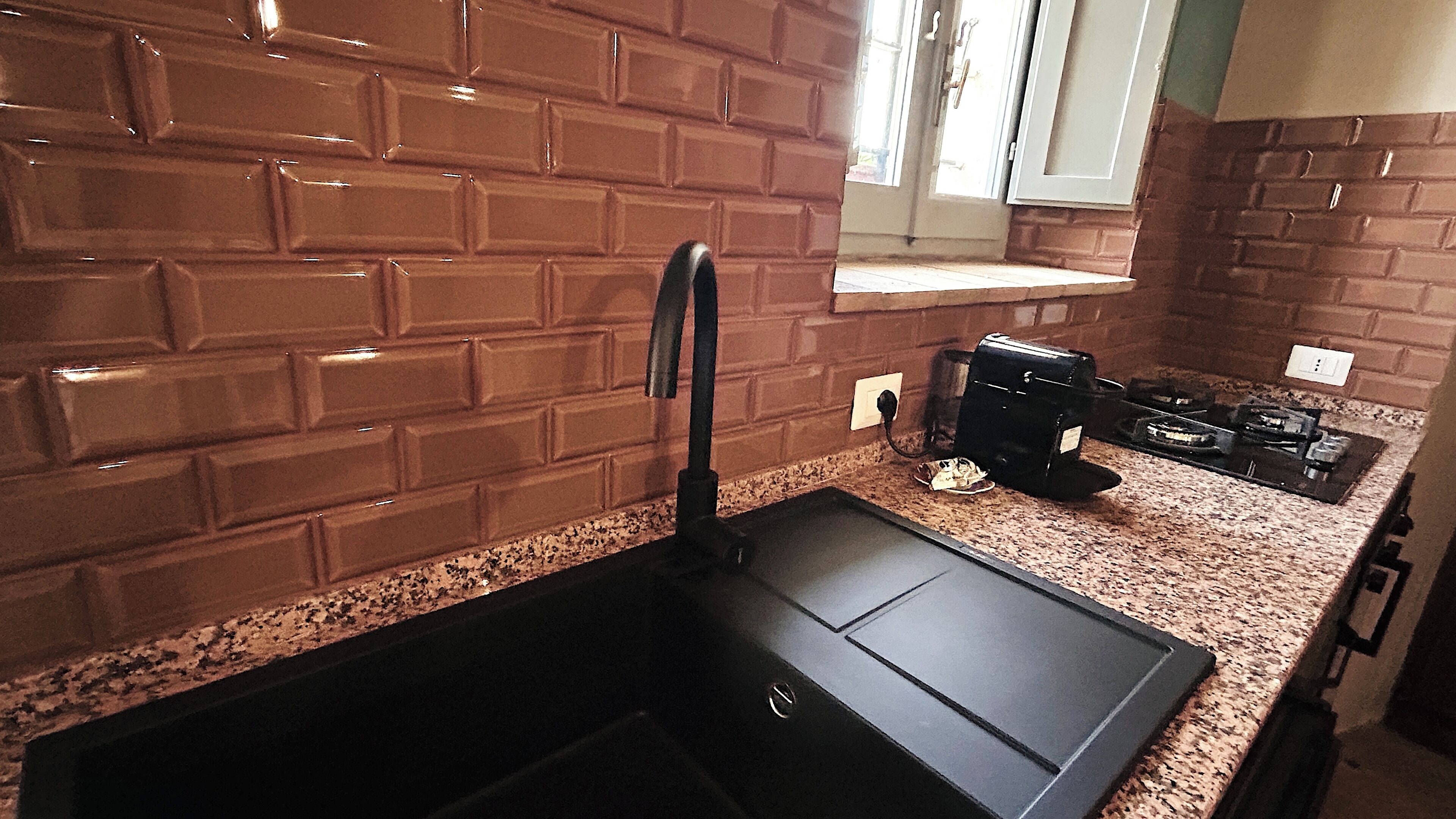 Eine Küche mit einem schwarzen Spülbecken, einer Arbeitsplatte aus Granit und einer Küchenwand mit Backsteinverkleidung.