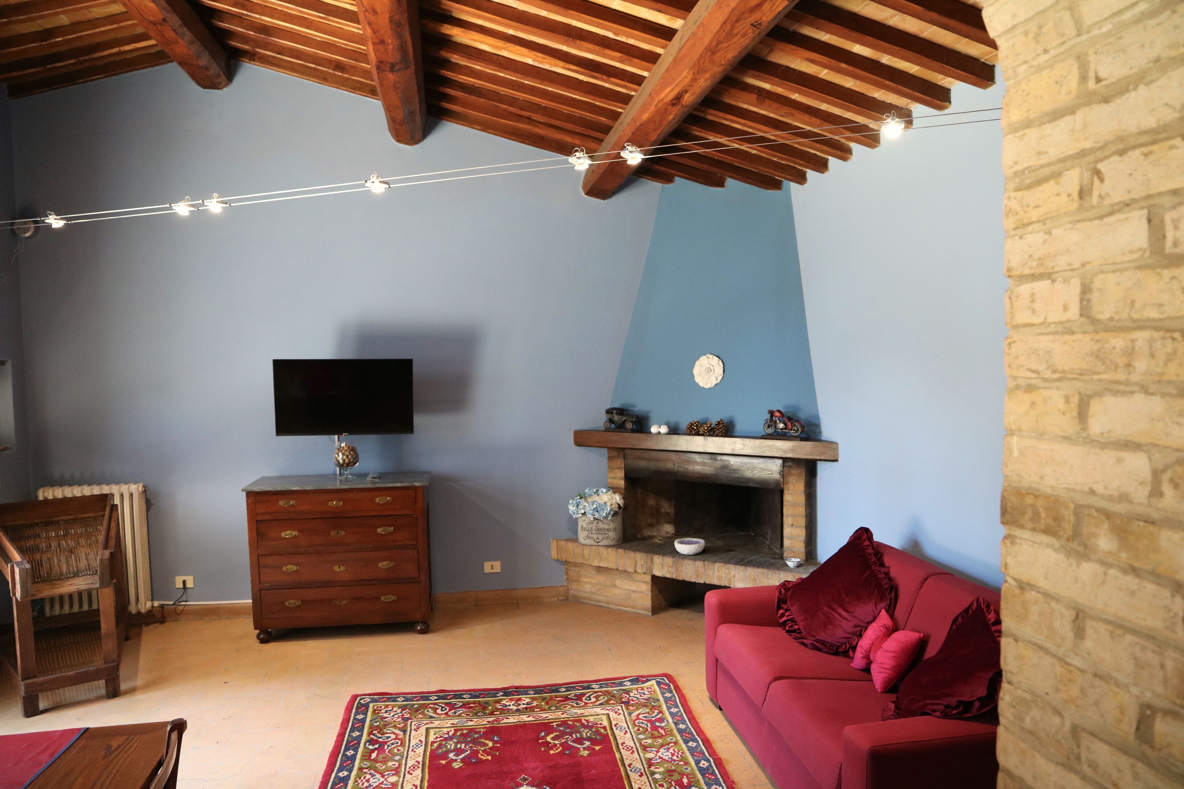 A living room with a fireplace, a television, a red sofa, and a wooden ceiling.