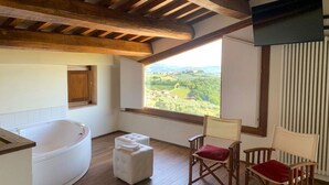 A room with a large bathtub, two ottomans, and two wooden chairs with cushions. - Corte Fratini Residenza D'Epoca (Trevi)