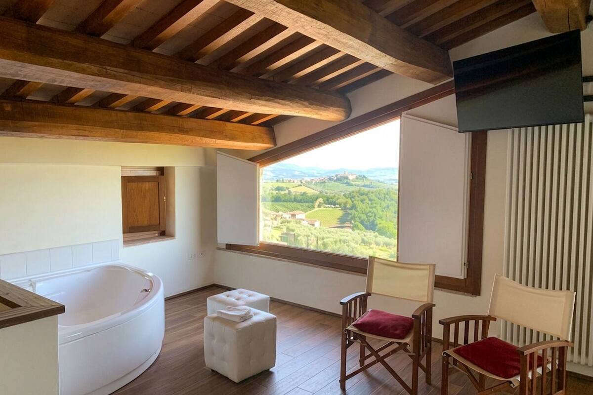 Una habitación con una bañera grande, dos otomanes y dos sillas de madera con cojines.