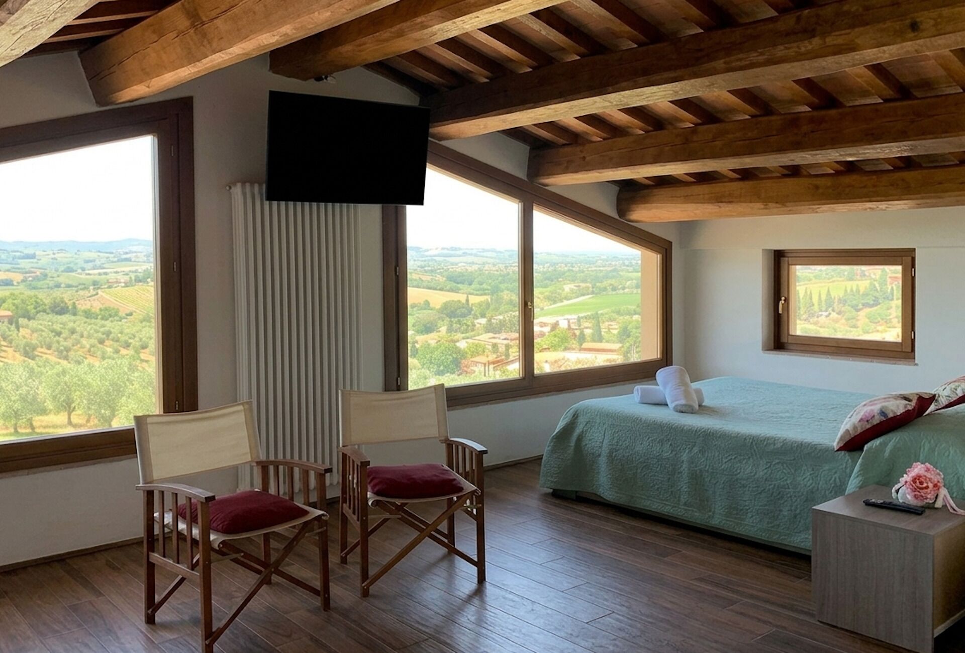 Une chambre avec un lit, deux fauteuils, une télévision et de grandes fenêtres donnant sur la campagne.
