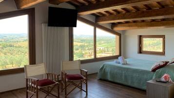 Une chambre avec un lit, deux fauteuils, une télévision et de grandes fenêtres donnant sur la campagne.