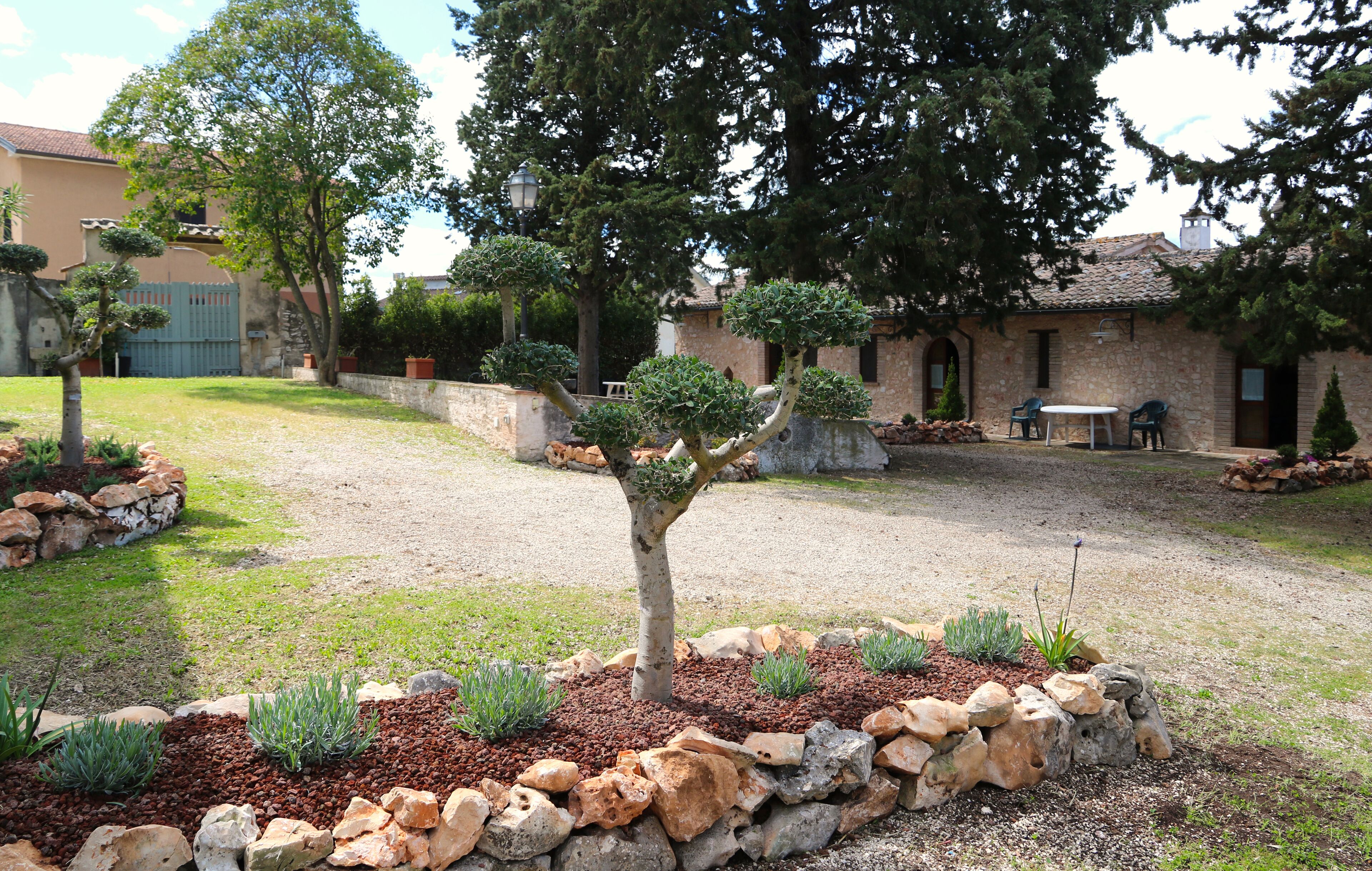 Un patio con muro de piedra, un árbol y un edificio con tejado de tejas.