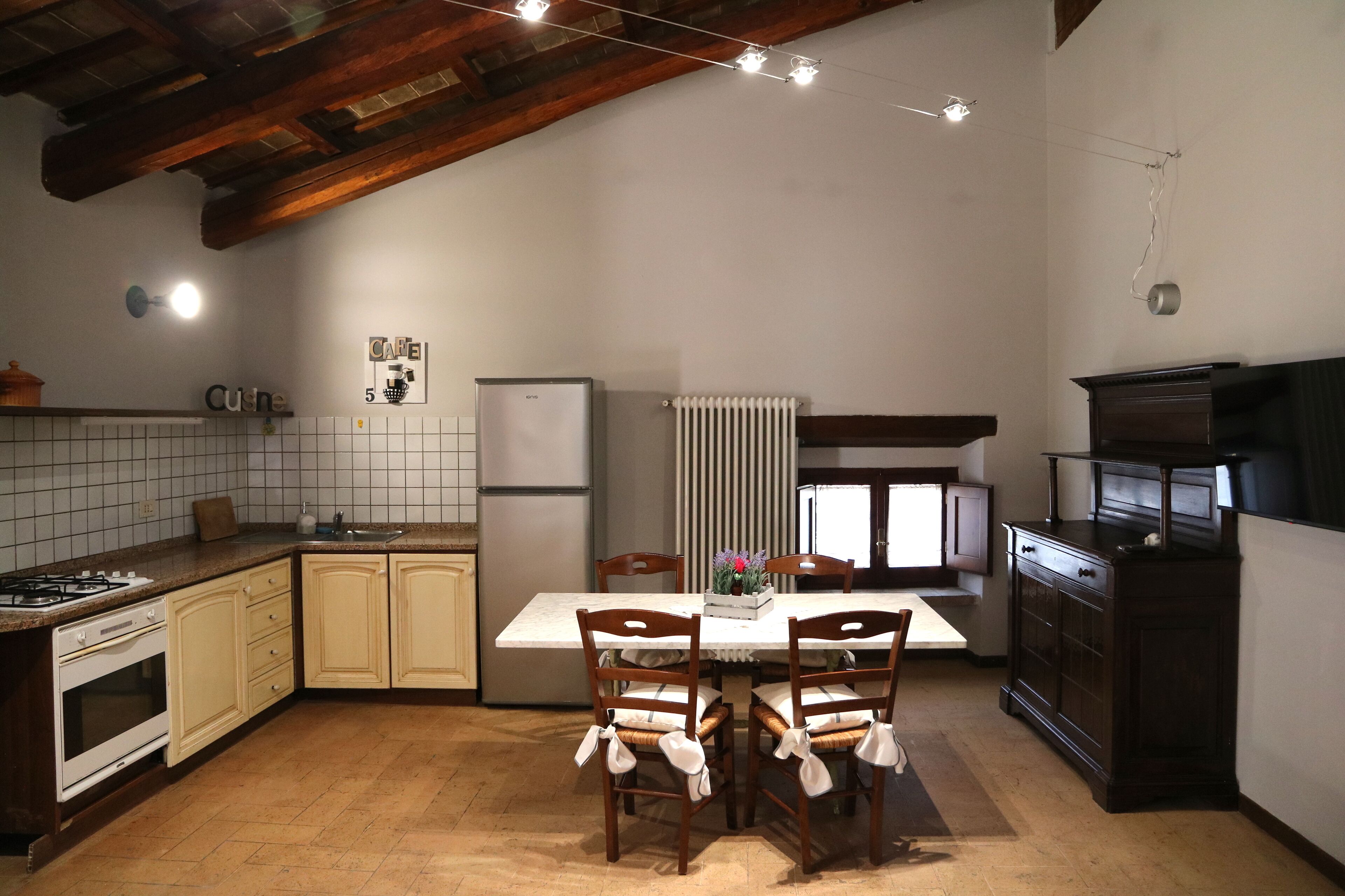 Una cocina con una mesa de comedor, sillas de madera, un refrigerador, una estufa y un armario.