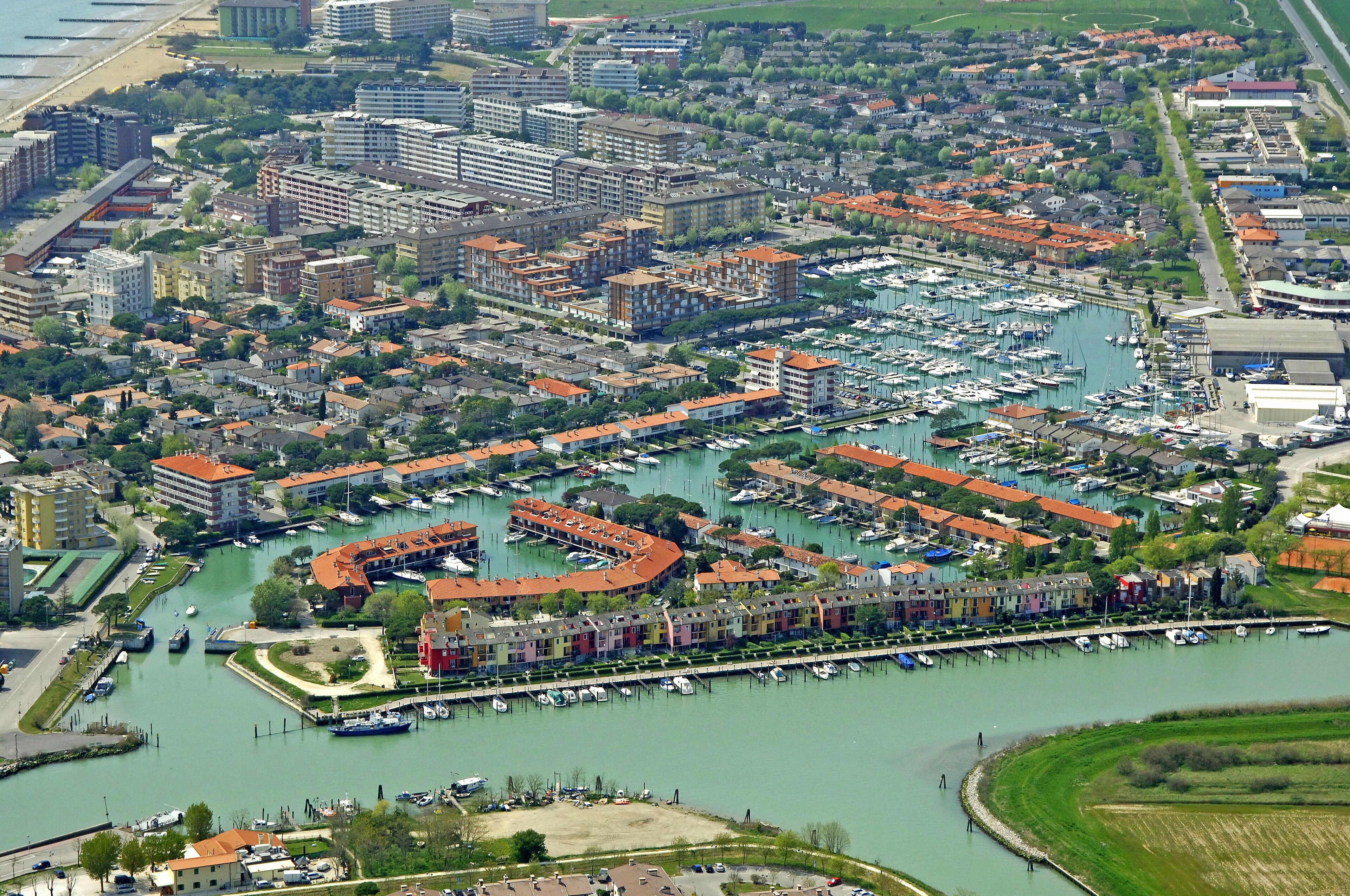 Vista aèria d'una marina amb vaixells, envoltada d'edificis residencials i una platja.