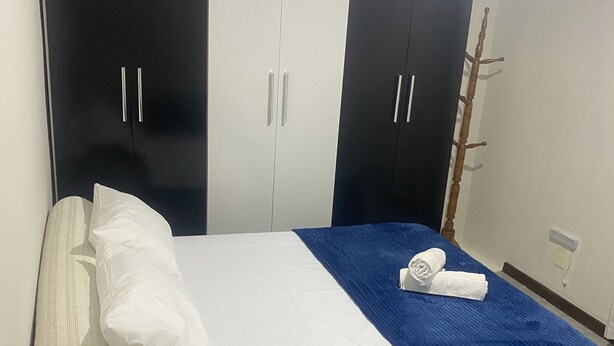 Een slaapkamer met een bed, nachtkastje, lamp, kledingkast en kapstok.