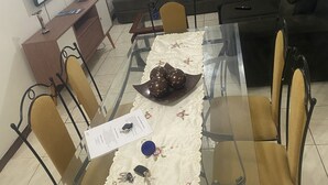Een eethoek met een glazen tafel, stoelen, een decoratief bord en een afstandsbediening op de bank.