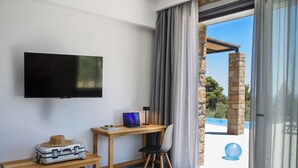 A room with a flat-screen TV, a wooden desk with a laptop, a suitcase, and a chair. - The Mavrolitharo Residence, new stone built villa.  (Chalkidiki)