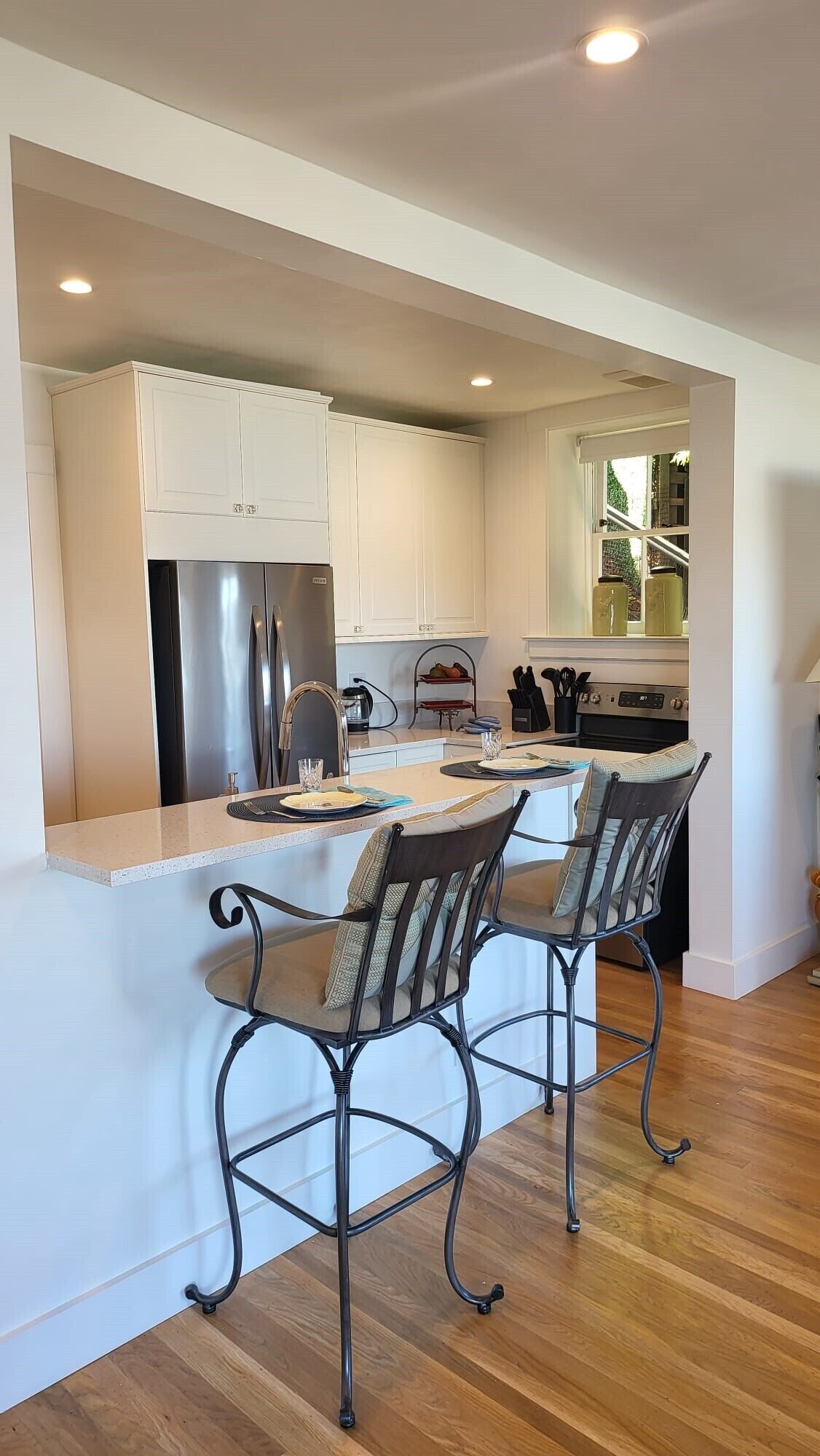 A modern kitchen with white cabinetry, stainless steel appliances, and a central island with bar stools.
