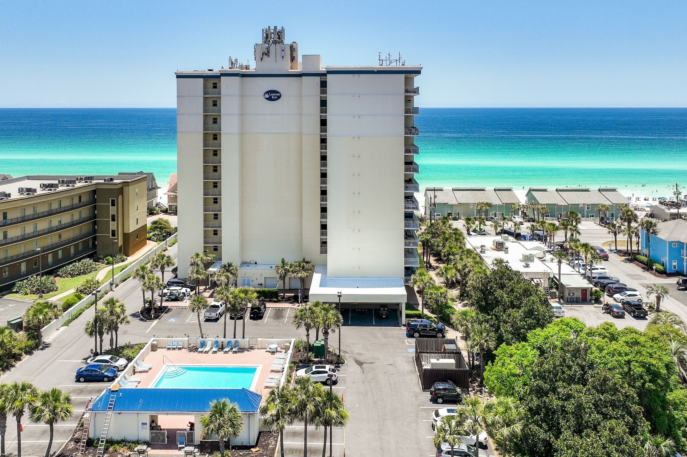 Ein Hochhaus-Hotel mit Pool und Blick auf den Strand, umgeben von Parkplätzen und Palmen.