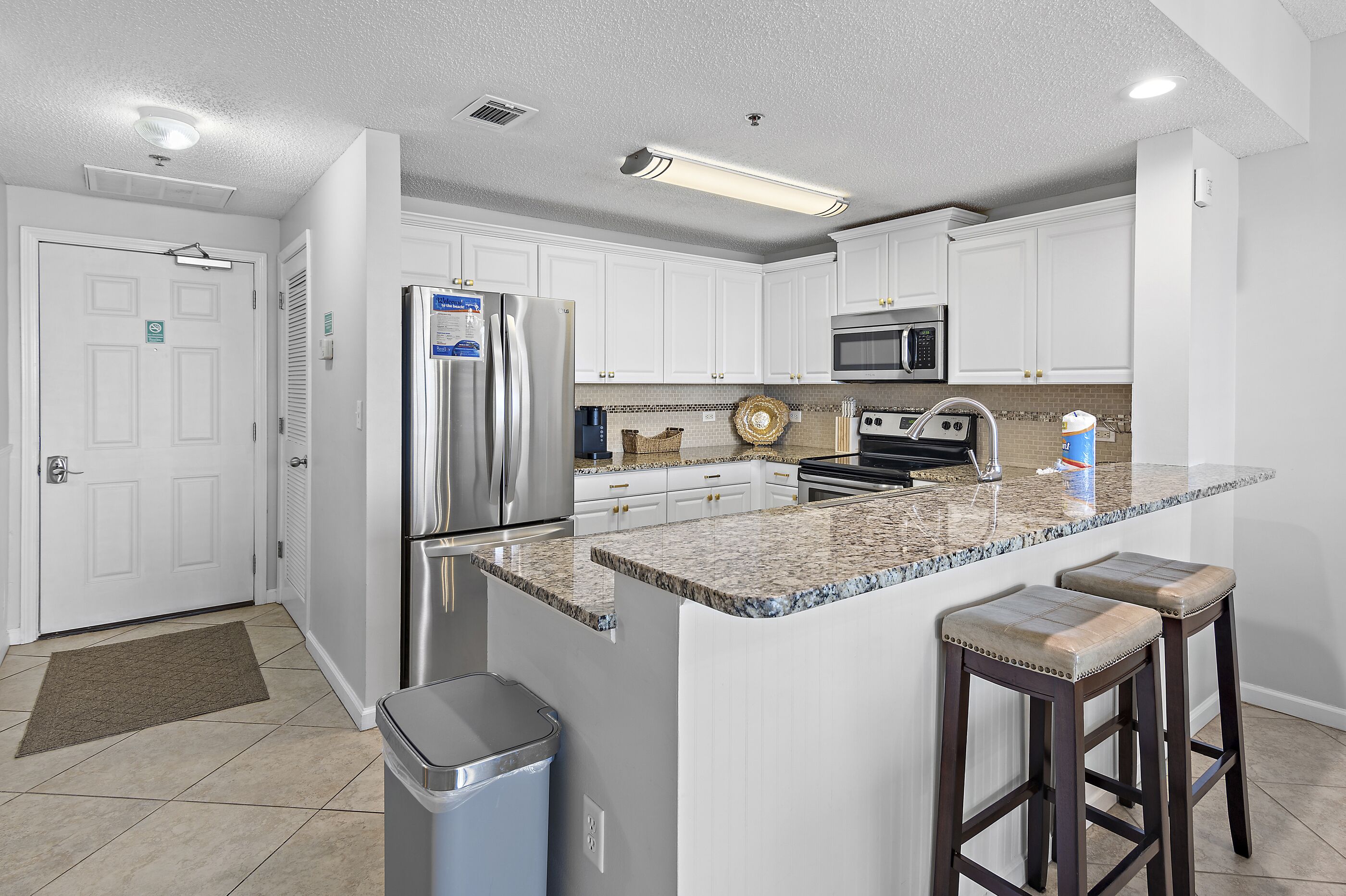 A modern kitchen with white cabinets, stainless steel appliances, a granite countertop, and two bar stools.