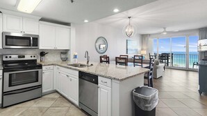A modern kitchen with white cabinets, stainless steel appliances, a granite countertop, and a view of the ocean through large windows. - 🌴FAB Gulf Views~Monthly Discount~Walk2Beach~2 Pools~2BR Leeward Key 505🌴 (Miramar Beach)