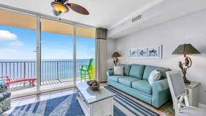 Un balcon avec vue sur la mer, un canapé de couleur turquoise, une table basse blanche et deux lampes fixées au mur.