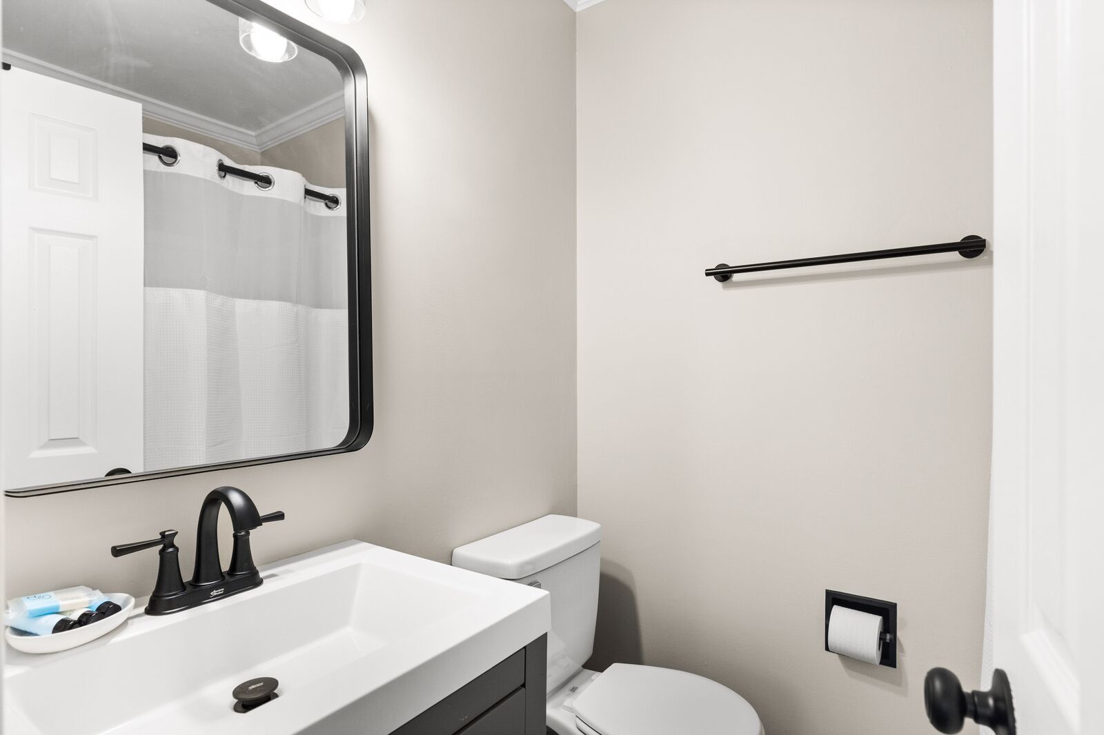 A bathroom with a white sink, black faucet, white toilet, and a towel rack.