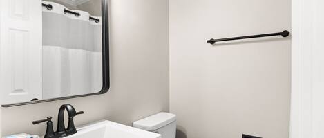 A bathroom with a white sink, black faucet, white toilet, and a towel rack.