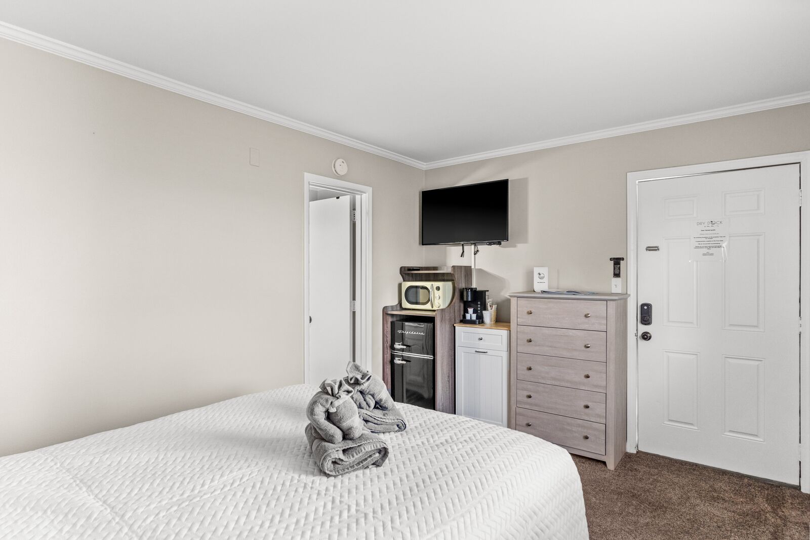 A hotel room with a bed, a TV mounted on the wall, a microwave, a coffee maker, a mini fridge, and a dresser.