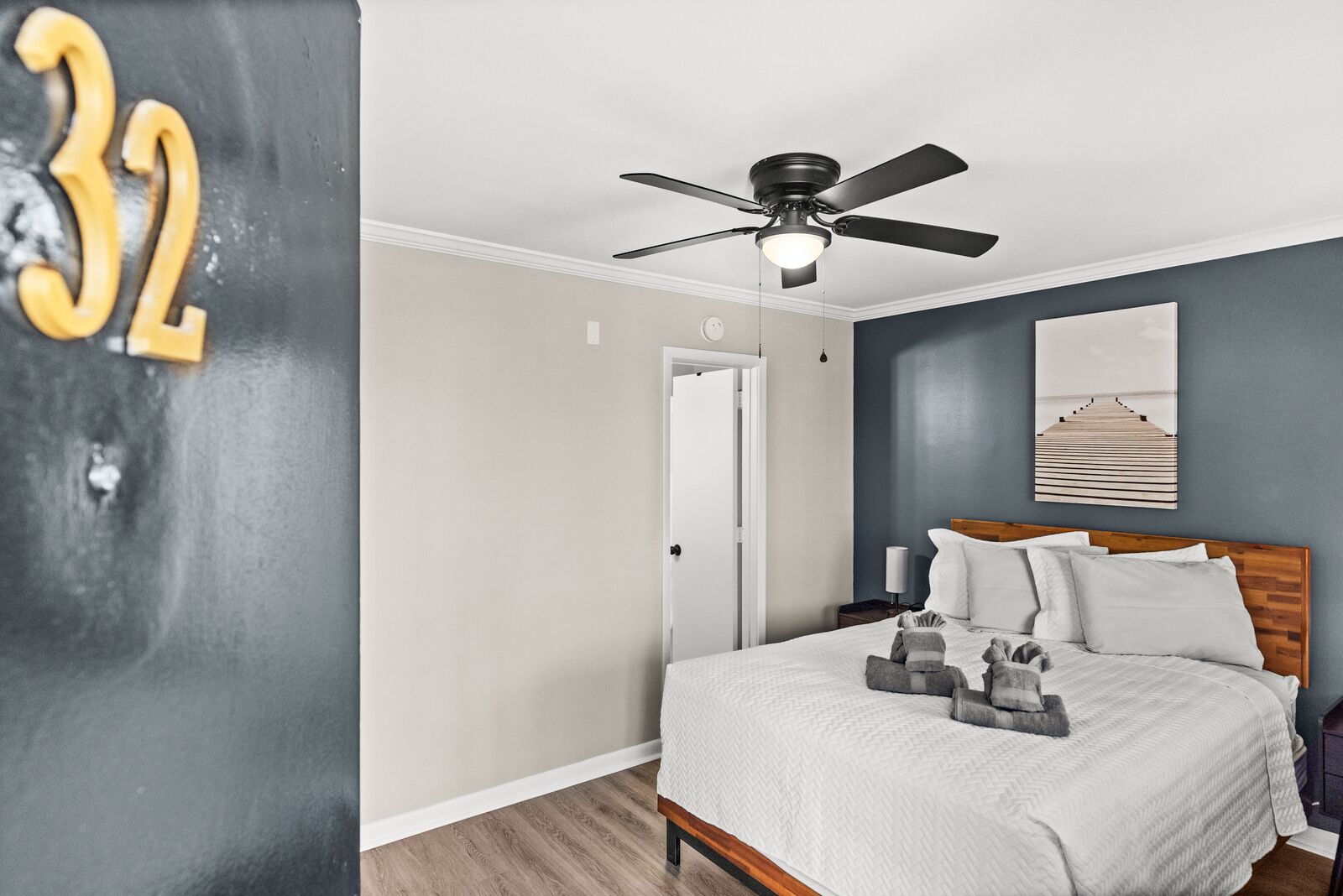 A bedroom with a bed, a ceiling fan, a nightstand, and a painting on the wall.