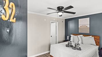A bedroom with a bed, a ceiling fan, a nightstand, and a painting on the wall.
