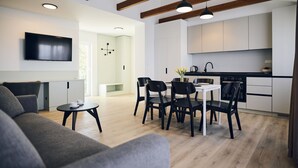 A modern kitchen with white cabinets, a black countertop, and a dining area with a table and chairs. - Malinska Green Apartments (Malinska-Dubasnica)