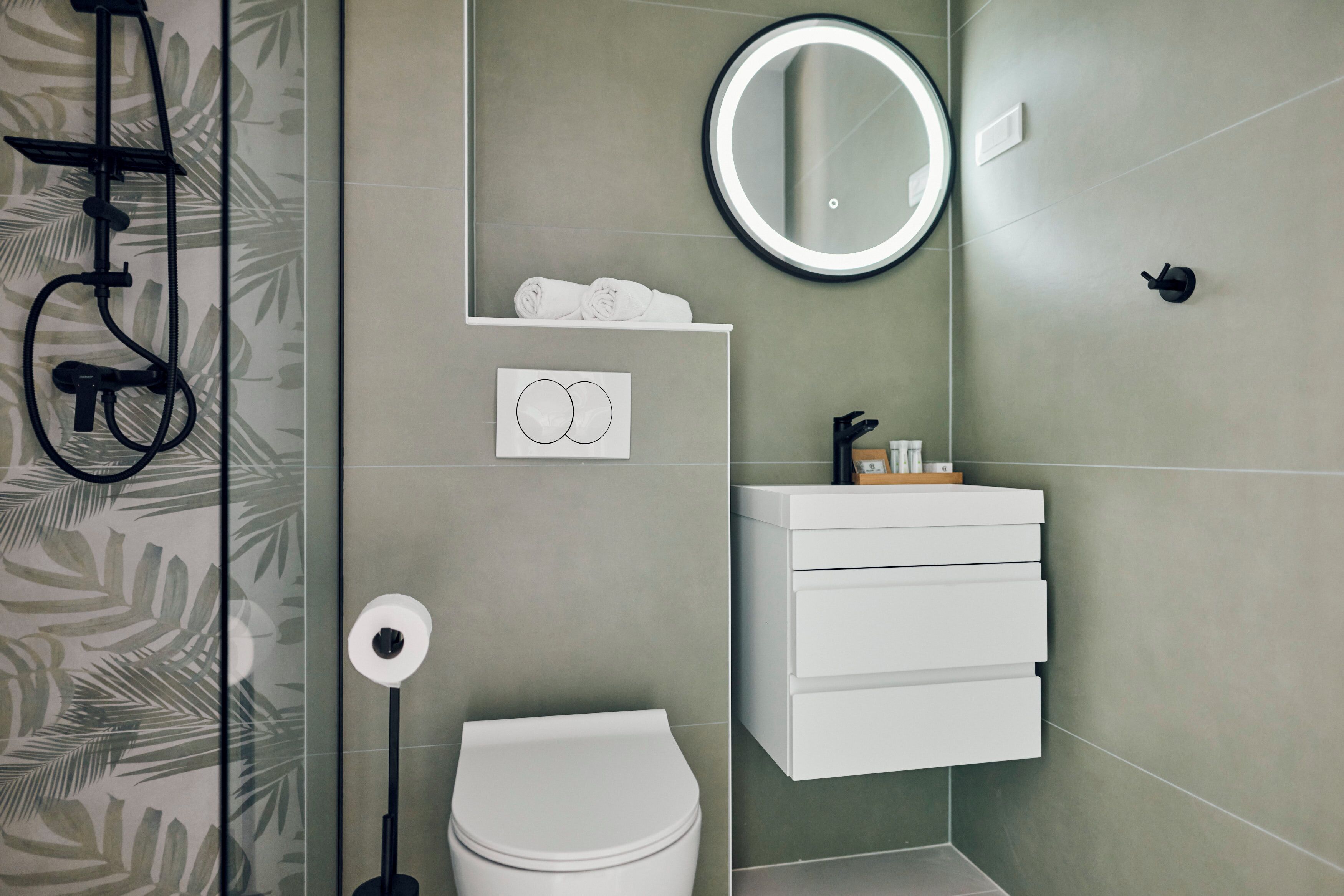 Ein modernes Badezimmer mit Toilette, Waschbecken, Spiegel und Dusche mit Handtuchhalter.